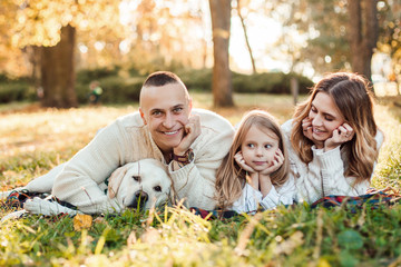 Obraz premium Happy family is having fun with dog labrador are lying on green grass in park.