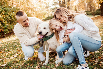 Fototapeta premium Happy beautiful family with dog labrador is having fun are sitting on green grass in park.