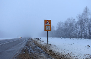 Foggy morning on the highway. Hazard warning sign on the sidelines.