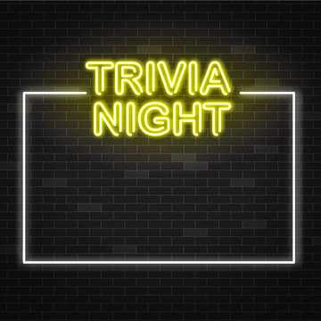 Trivia night yellow neon sign in white frame on dark brick wall background with copy space.