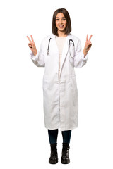 A full-length shot of a Young doctor woman smiling and showing victory sign with both hands over isolated white background