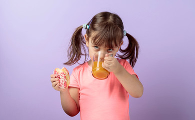 Four-year-old girl in a pink t-shirt eat donut and drink juice.