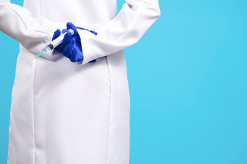 Close up photo of young doctor hands in gloves holding syringe over blue background.