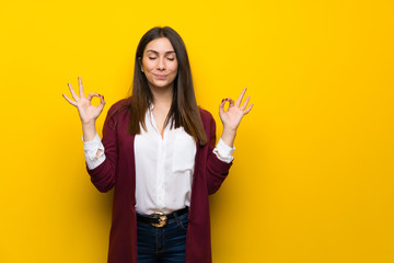 Young woman over yellow wall in zen pose
