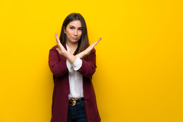 Young woman over yellow wall making NO gesture
