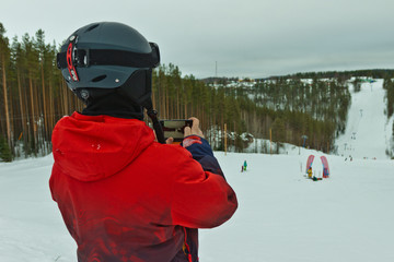 snowboarder in a red jacket, in a helmet and goggles shoots a ski slope on a smartphone