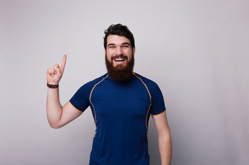 Fototapeta premium Portrait of an happy bearded man pointing finger up at copyspace isolated over gray background