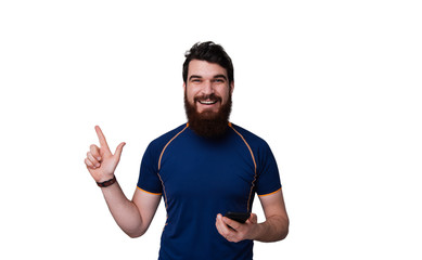 Bearded man in blue tshirt holding mobile phone while pointing up with finger over white background