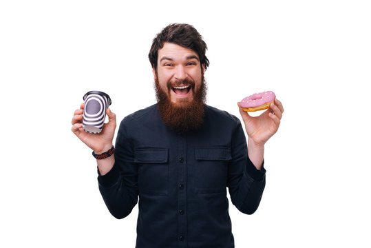 Excited Young Bearded Man Holding Glazed Donut And Cup Of Coffee  Isolated On White Background