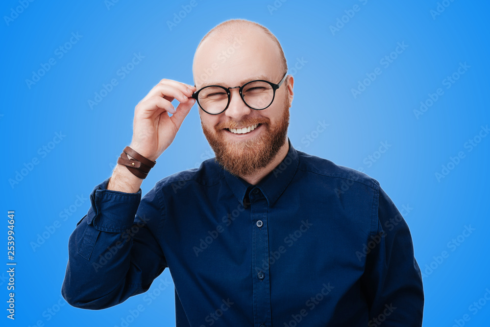 Wall mural photo of cheerful smiling young businessman touching his glasses over blue background