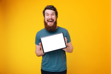 Excited young bearded man showing white blank of tablet screen and lookiing at camera