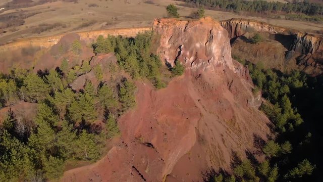 Drone descending into the crater of Racos Volcano gives a sense of the size of the remains of this dead volcano. Tress grow inside on the red soil and countryside revealed as camera tilts up.