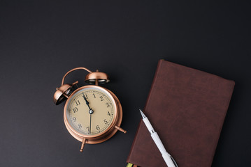 Flat lay concept, workplace of the writer, vintage clock, notebook  and pencil, on black table background