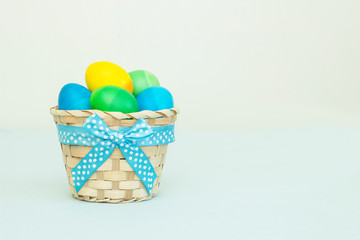 Ombre colored Easter eggs in a wicker basket with blue ribbon and copy space