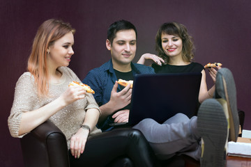 Obraz na płótnie Canvas Young people eating pizza at the laptop. A man and two women are watching a movie on a computer.
