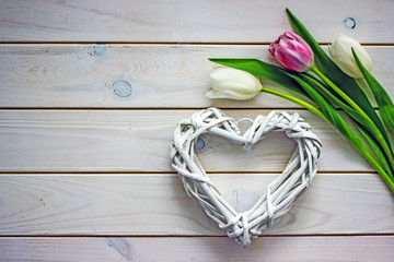 Obraz premium Heart and flowers background. White wicker heart and pink tulips on wooden background, top view, flat lay, copy space Concept of valentine's day, mother's day, background about love