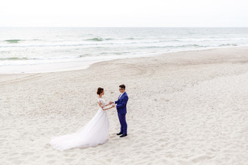 newlyweds walking along the sea beach at the wedding. The groom hugs the bride