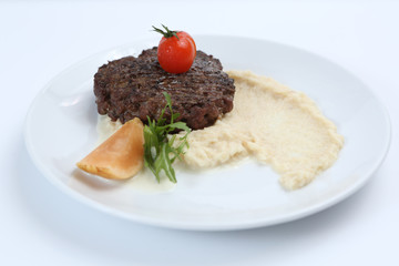 fried meat cutlet on a plate, with celery puree, garnished with tomato cherry and sour apples, isolated