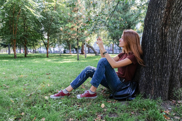 Hipster using her smartphone. Young successful woman doing selfie in a park in nature. Girl taking pictures of their friends on smartphone.