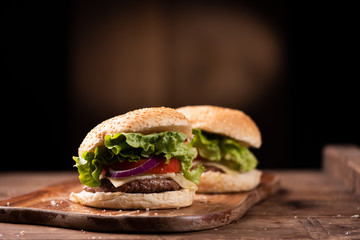 Tasty grilled beef burger with lettuce, cheese and onion served on cutting board with copyspace