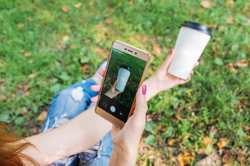 Hipster girl using her smartphone. Young successful woman sitting on social networks and read messages. Girl takes a picture of their sneakers and coffee on a mobile phone.