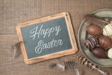 Easter holiday background with brown easter eggs decorations and chalkboard on wooden table.