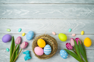 Easter holiday background with easter eggs in bird nest and tulip flowers on wooden table.