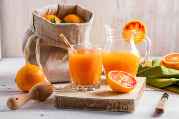 Glass of fresh pressed orange juice and blood oranges on wooden table. Bright summer mood.