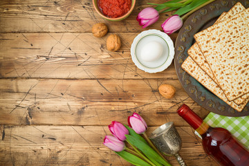 Fototapeta na wymiar Jewish holiday Passover background with matzo, seder plate, wine and tulip flowers on wooden table.