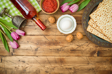 Jewish holiday Passover background with matzo, seder plate, wine and tulip flowers on wooden table.