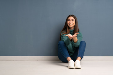 Young woman sitting on the floor holding copyspace imaginary on the palm to insert an ad