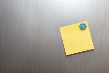 Yellow notepad on refrigerator with magnet of heart idea for note,memory,reminder,information,