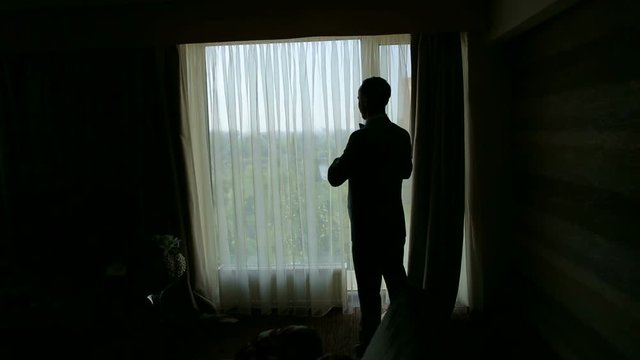 Silhouette of a successful young man puts on a suit jacket in the morning. Businessman puts on a jacket. Morning of the groom.