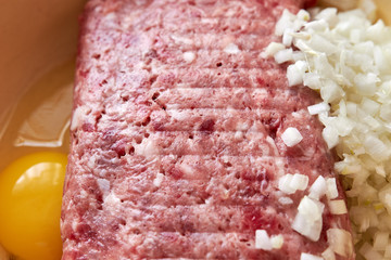 fresh beef and pork minced meat sprinkled with white onions and chicken egg for making cutlets and schnitzel in a yellow iron plate