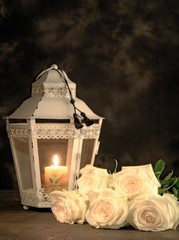 Beautiful white roses and candle on table against black background