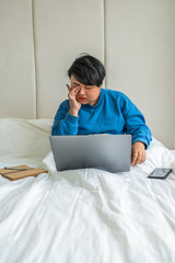 Vertical photo of tired Asian businesswoman sitting on bed