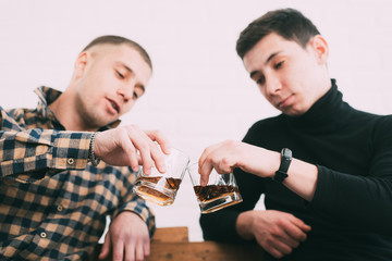 two men drink whiskey sitting on a wooden couch