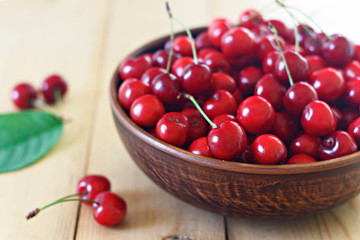 Cherry berries and leaves in a brown plate on a wooden background. Summer berries. Cherry spread out on a light background