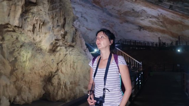 Pretty woman with photo camera walking and exploring through a giant Paradise Cave in Phong Nha Ke Bang National Park, Vietnam.