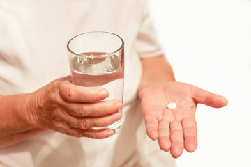 old hands are holding pills and a glass of water, medicine for an elderly woman, to drink a pill