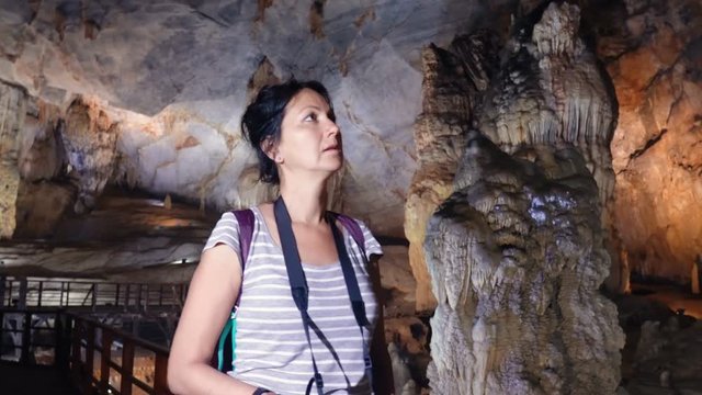 Pretty woman with photo camera walking and exploring through a giant Paradise Cave in Phong Nha Ke Bang National Park, Vietnam.