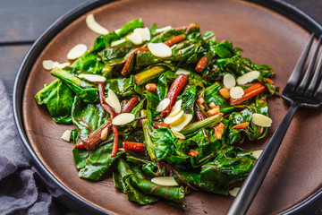 Beet greens salad with nuts in black plate. Healthy vegan food concept.
