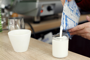 Barista on wooden bar table in cafe pours milk in glass for preparing latte