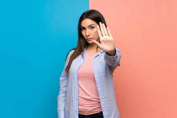 Young woman over pink and blue wall making stop gesture denying a situation that thinks wrong