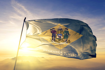 Delaware state of United States flag waving on the top sunrise mist fog - obrazy, fototapety, plakaty