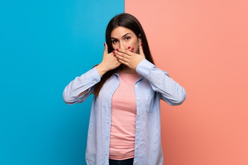 Young woman over pink and blue wall covering mouth with hands for saying something inappropriate