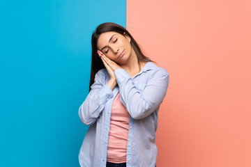 Young woman over pink and blue wall making sleep gesture in dorable expression