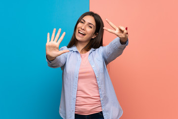 Young woman over pink and blue wall counting seven with fingers