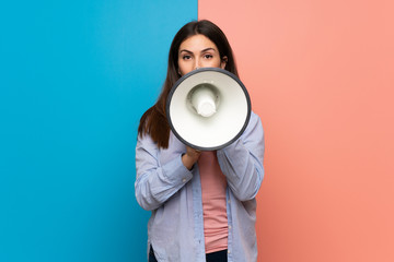 Young woman over pink and blue wall shouting through a megaphone