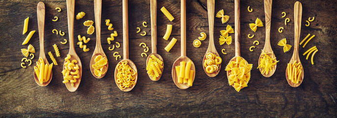 Various kinds of pasta in wooden spoons.